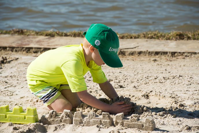 child in green long cove cap building sandcastle on shore of Cedar Creek Lake beach