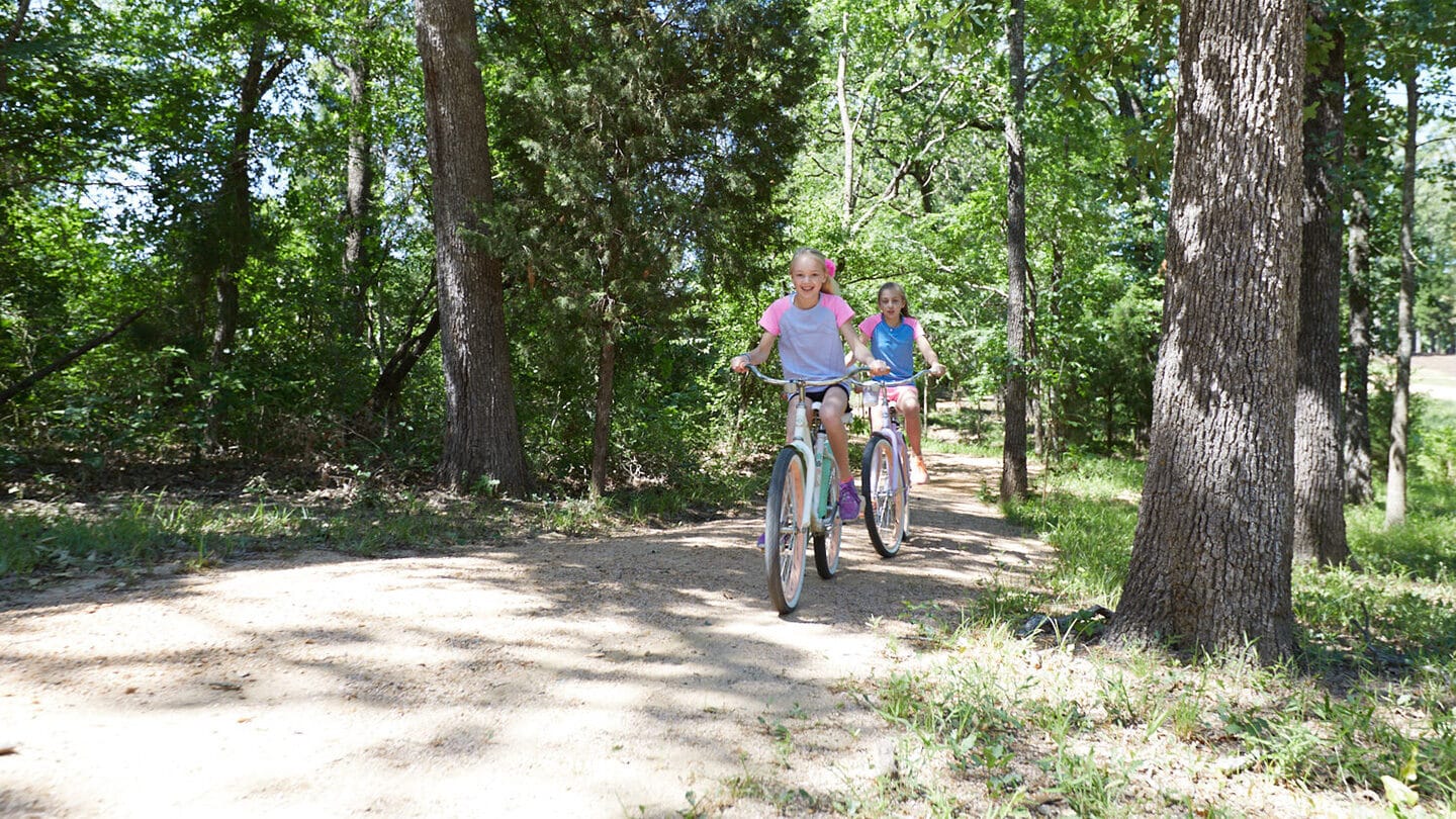 Blonde teenage girls riding bikes on trail in wooded area